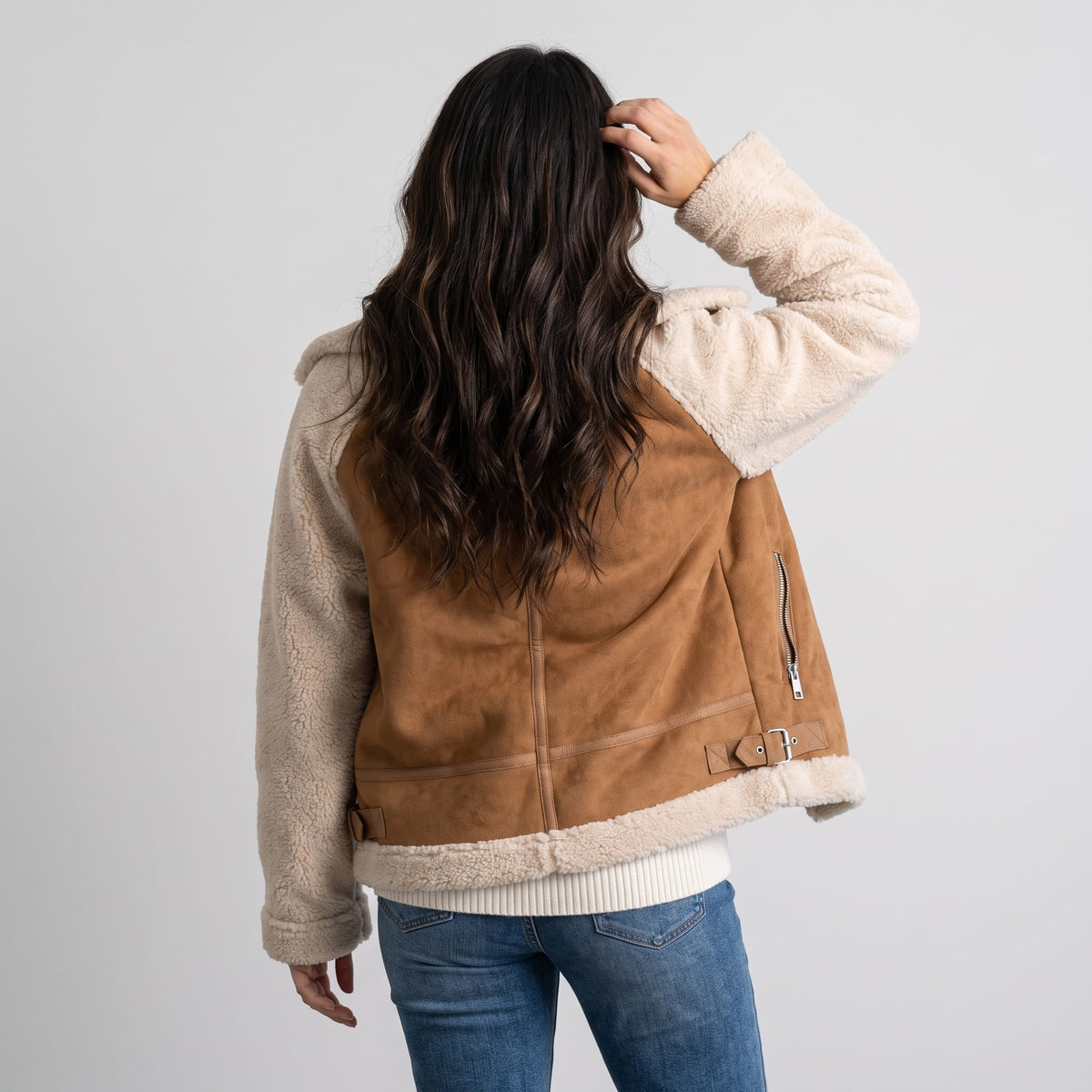 A woman wearing a beige and brown suede leather shearling aviator jacket, shown in side view