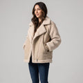 A woman wearing a beige suede leather shearling aviator jacket with an oversized lapel and sherpa trim
