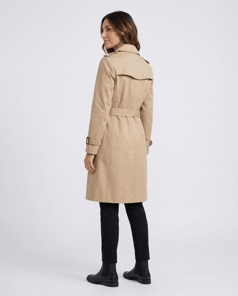 A woman wearing a beige mid-length trench coat, shown from the back with a belted waist