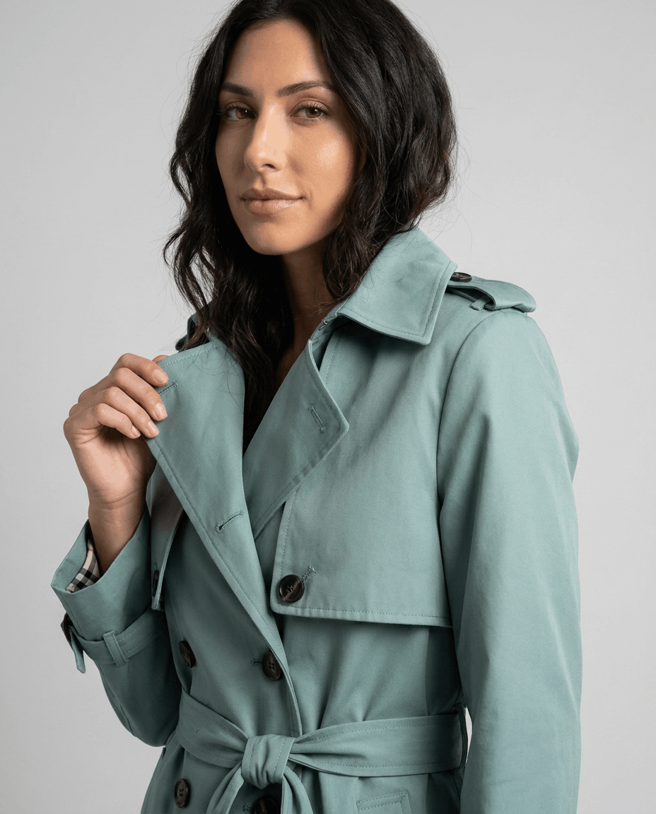 Close-up of a woman wearing a sage green mid-length trench coat with a lapel collar and belted waist