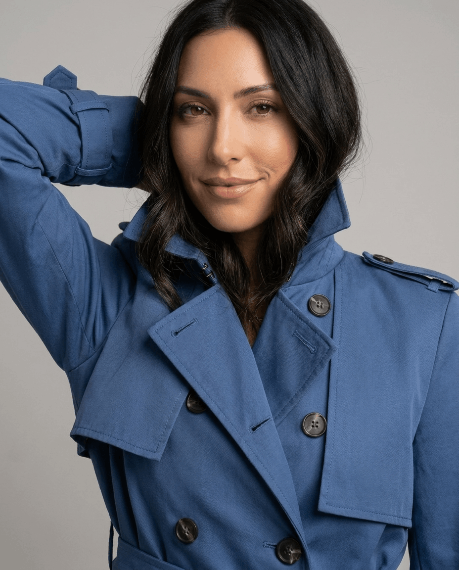 Close-up of a woman wearing a blue mid-length trench coat with a lapel collar and belted waist