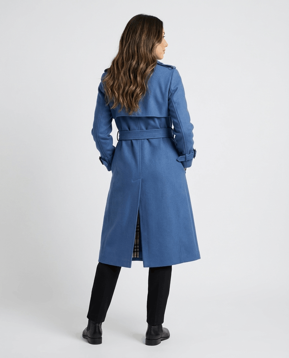 A woman wearing a blue mid-length trench coat with a belted waist, shown from the back