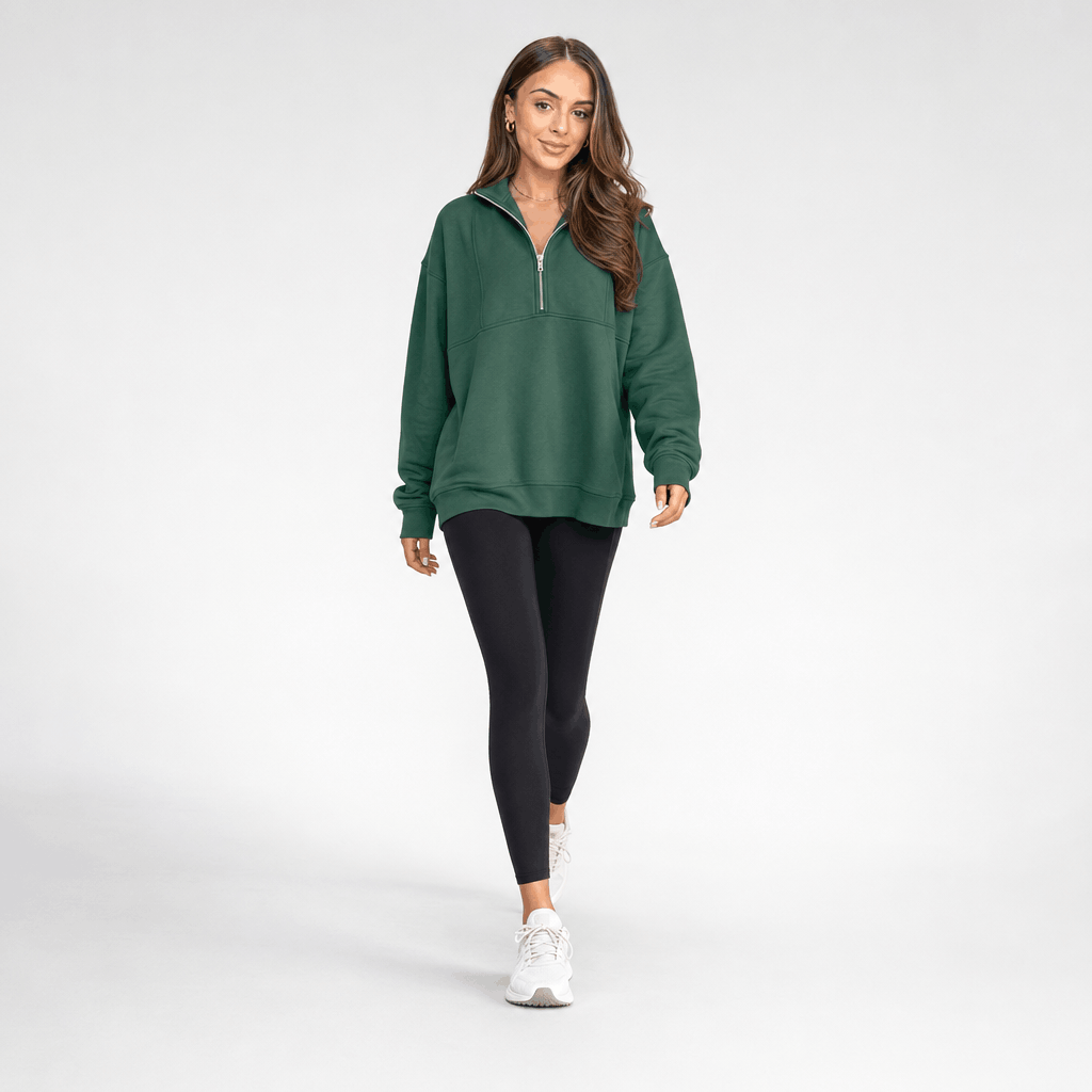 Full-body view of a female model wearing the dark green quarter-zip pullover with black trousers and white sneakers.