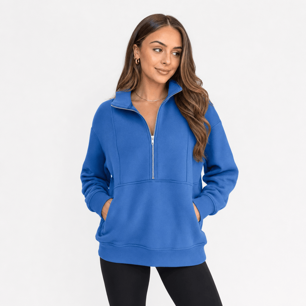 Female model wearing a bright blue quarter-zip pullover with black trousers.