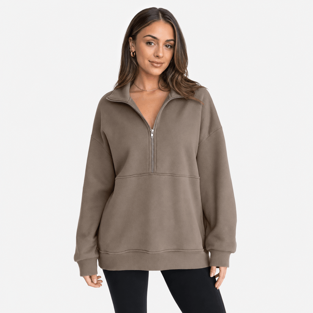 Female model wearing a taupe quarter-zip pullover with a relaxed fit and ribbed cuffs and hem, paired with black trousers.