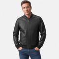 Male model wearing a black leather-style zip-up jacket with a stand collar, seam detailing, and zippered pockets, paired with blue jeans.