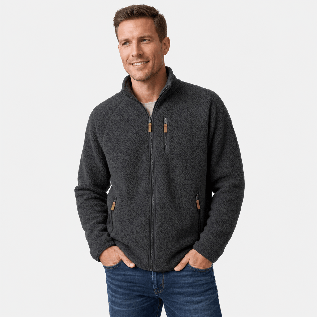 Male model wearing a dark charcoal zip-up fleece jacket with hands in his pockets.