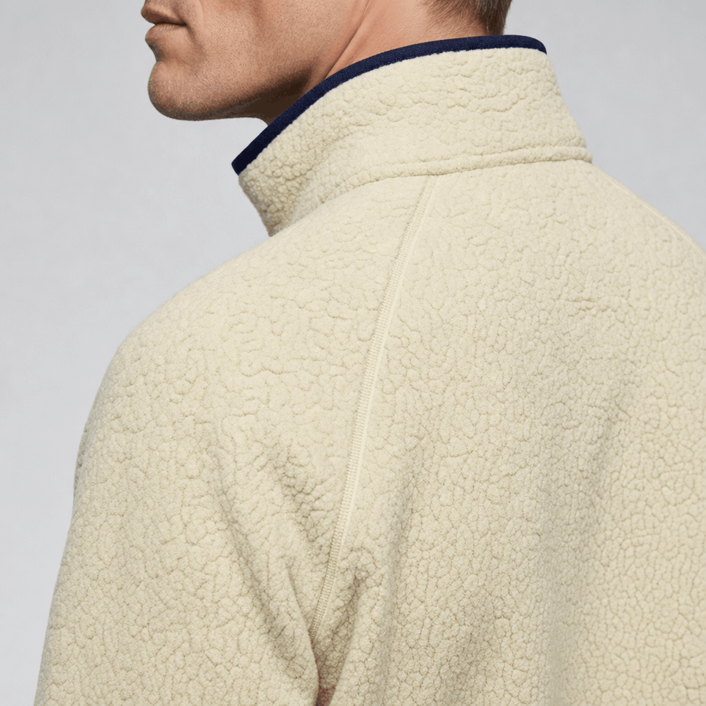 Back and side close-up of the cream fleece jacket, highlighting the high collar, dark trim, and textured fabric.