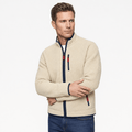 Male model wearing a cream fleece zip-up jacket with a high stand collar, dark trim, and contrasting zippered pockets, paired with blue jeans.
