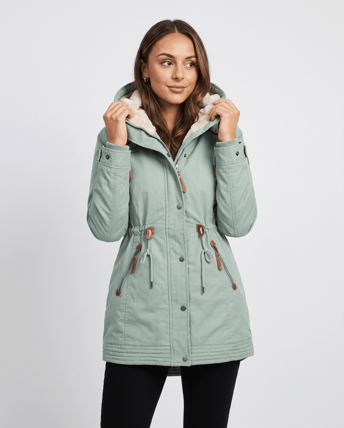 A woman wearing a light green winter parka jacket with a hood, plush lining, and drawstring waist