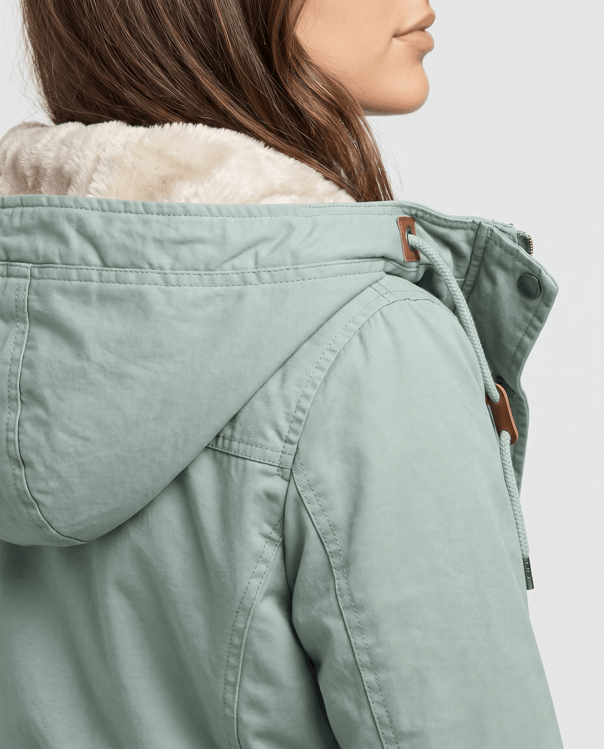 Close-up of a woman wearing a light green winter parka jacket, showing the plush-lined hood and drawstring waist