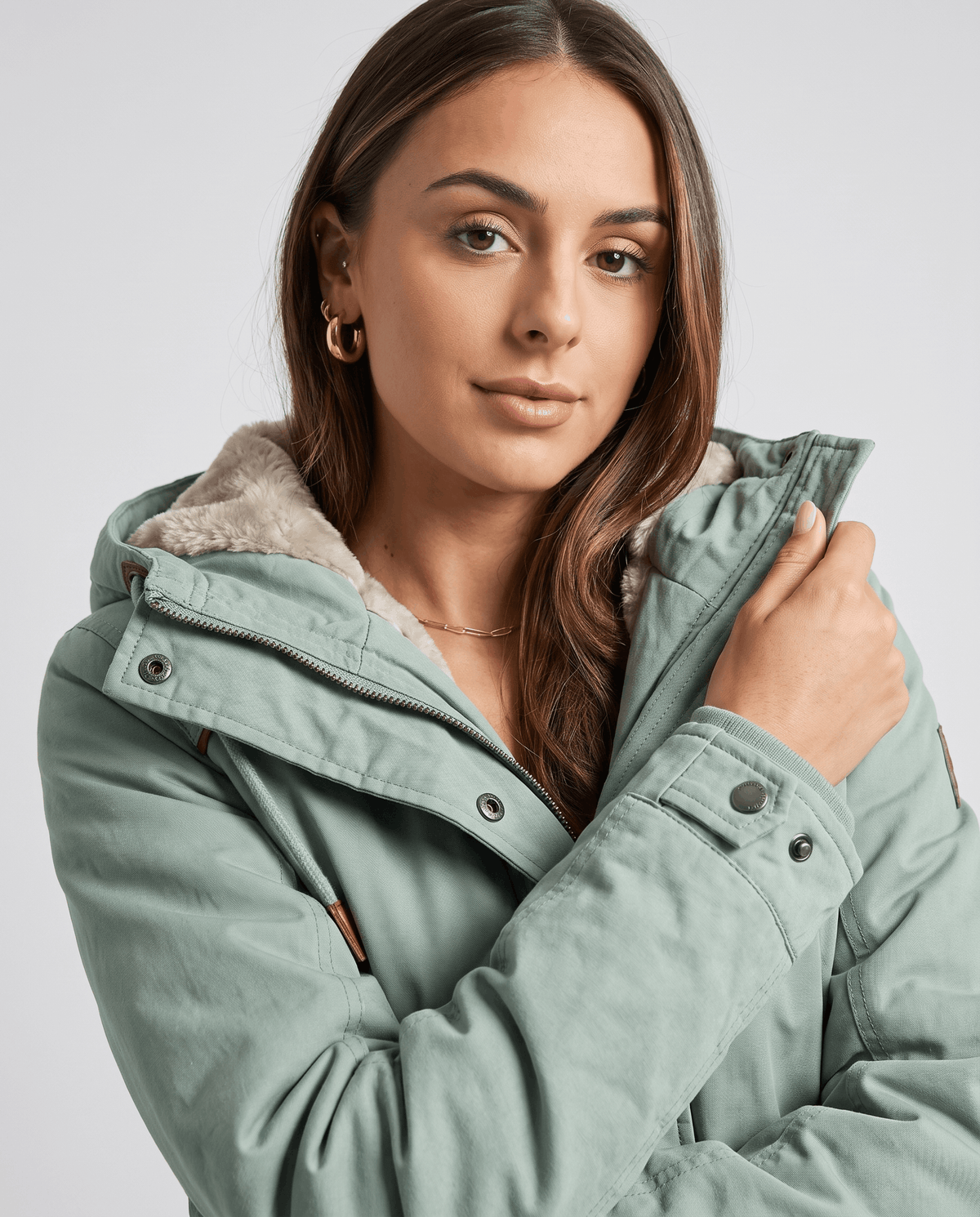 Close-up of a woman wearing a light green winter parka jacket, showing the plush lining, hood, and front details