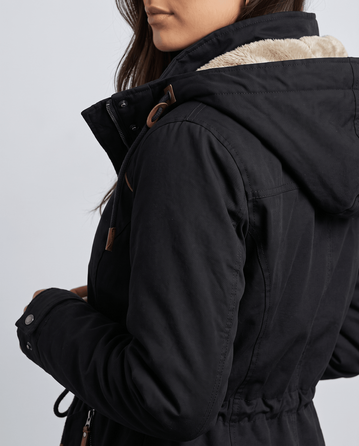 Close-up of a woman wearing a black winter parka jacket, showing the hood, plush lining, and side profile
