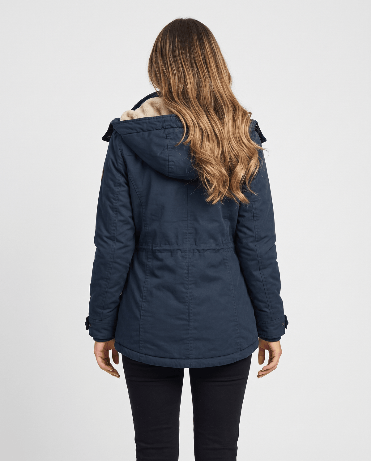 A woman wearing a navy blue winter parka jacket with a hood, plush lining, and drawstring waist, shown from the back