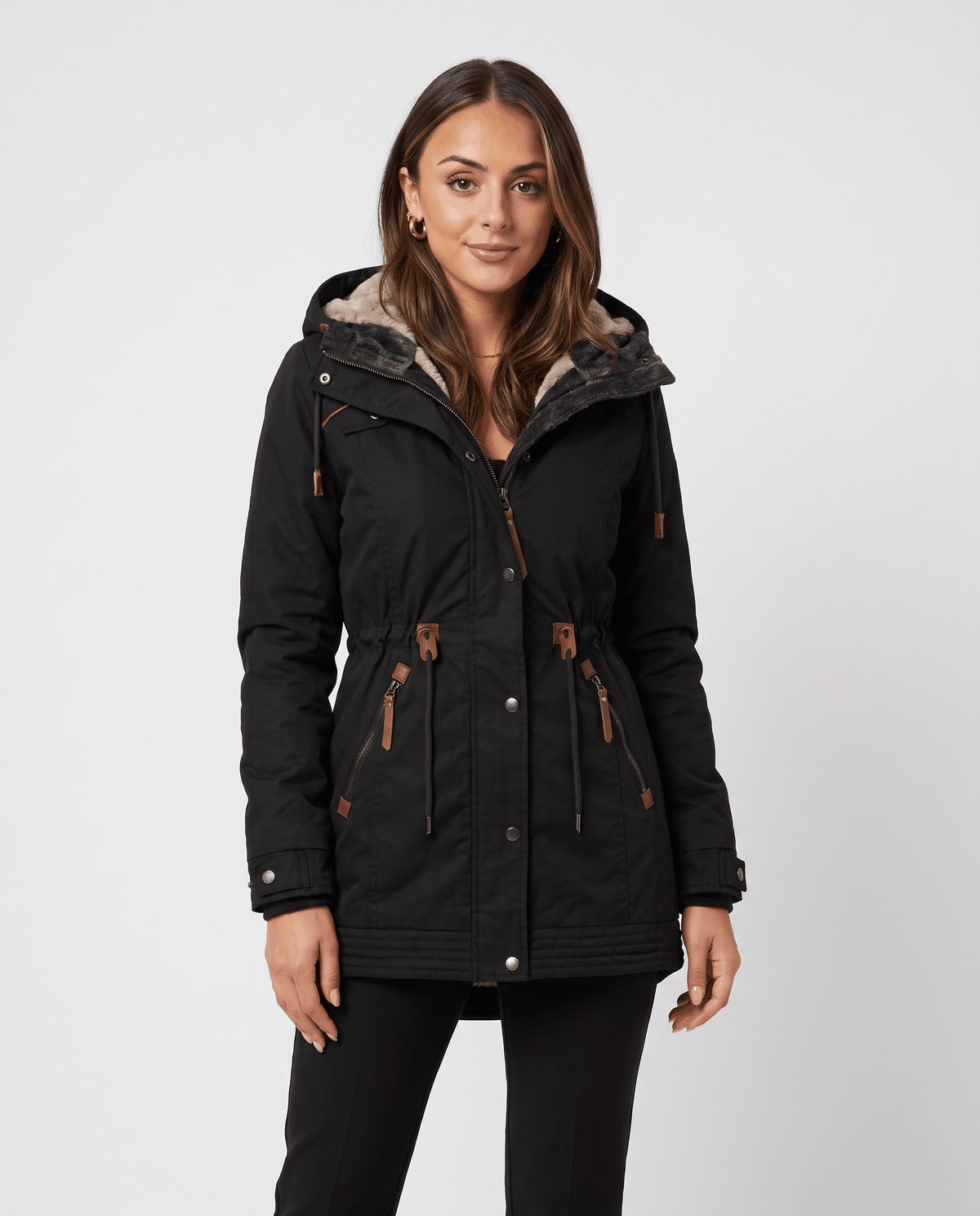 A woman wearing a black winter parka jacket with a hood, plush lining, multiple zip pockets, and a drawstring waist
