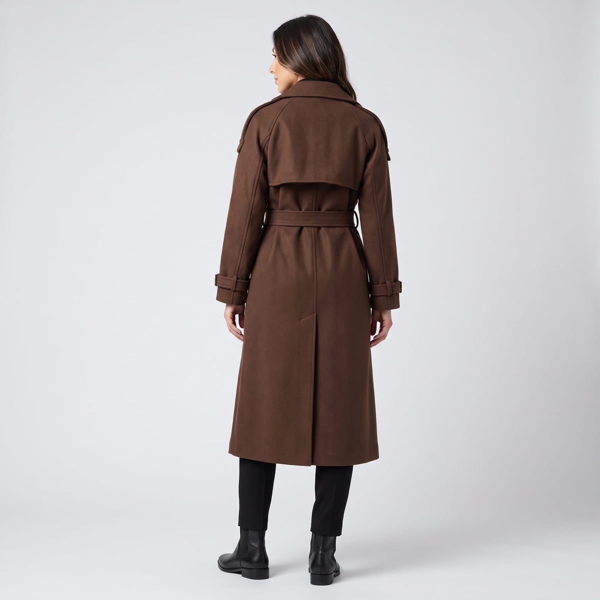 A woman wearing a brown wool trench coat with a double-breasted front and waist belt, shown from the back
