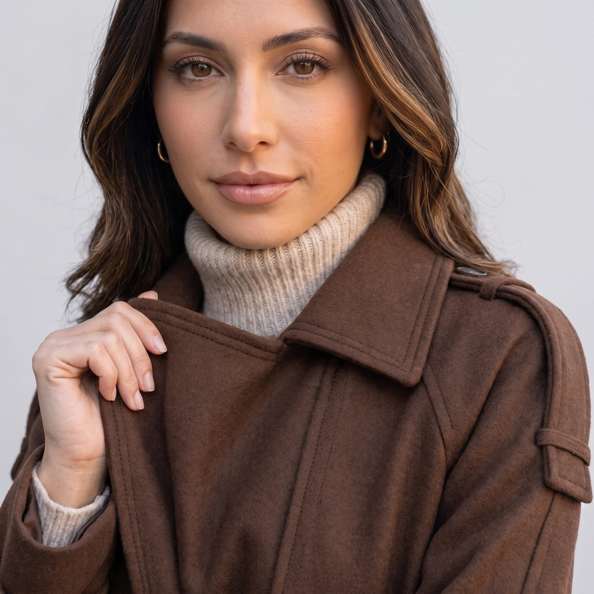 Close-up of a woman wearing a brown wool trench coat, showing the collar and double-breasted front