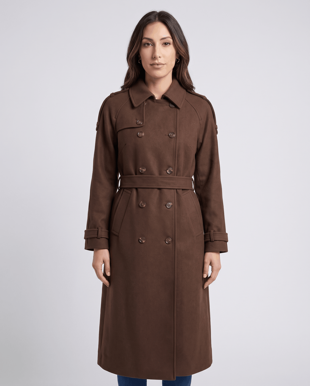 Brown belted double-breasted trench coat with notched collar and cuff straps, worn by a female model