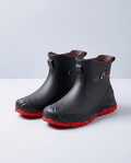 Pair of black rubber ankle rain boots with red non-slip lug soles on a white background