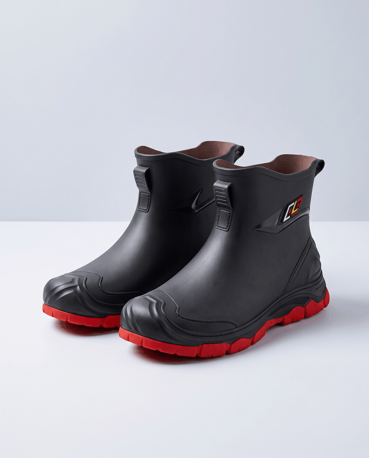 Pair of black rubber ankle rain boots with red non-slip lug soles on a white background