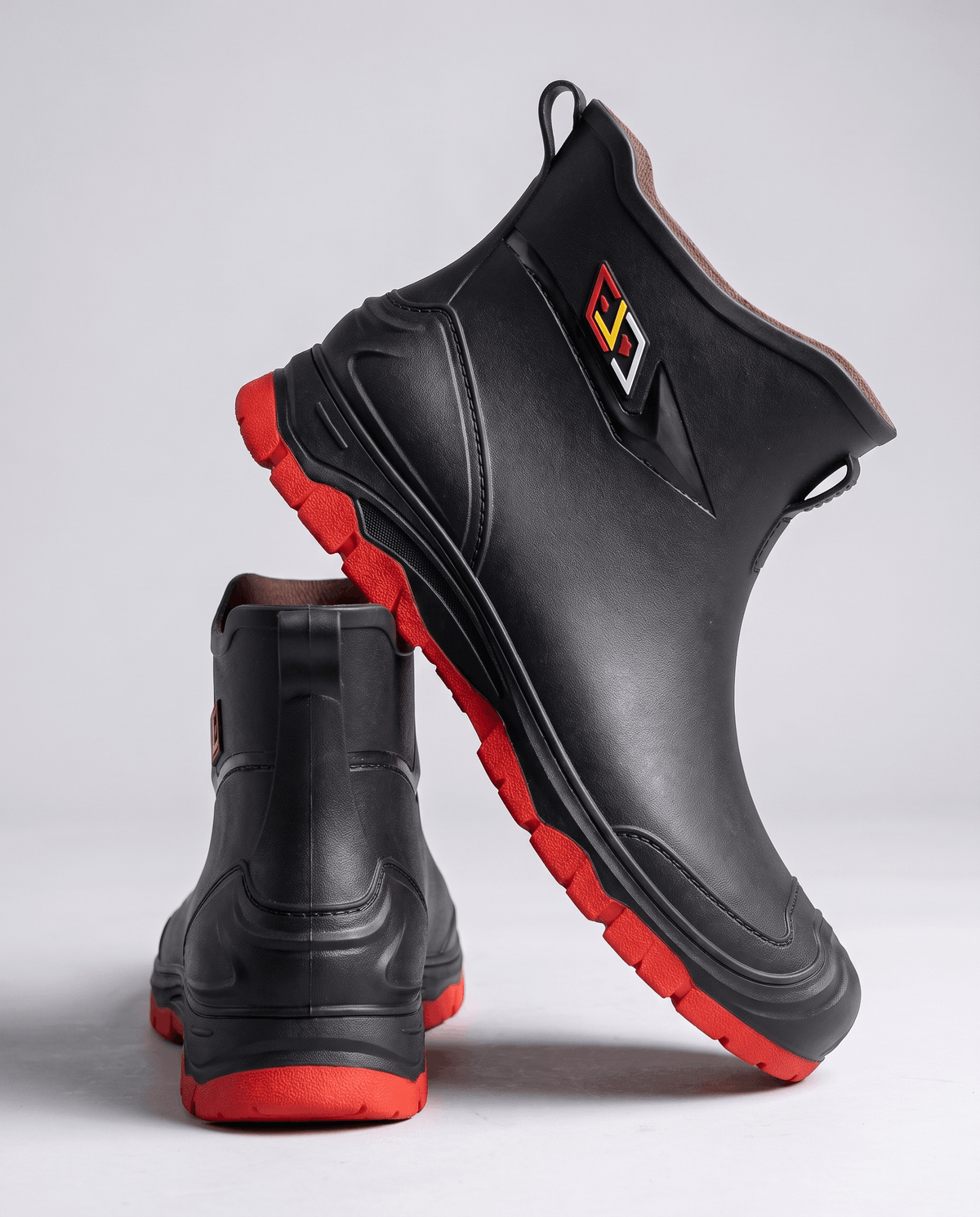 Black rubber boot tilted to show the red tread sole, second boot behind it