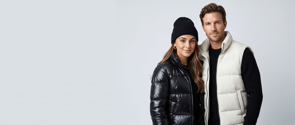 Couple in a black puffer jacket and an ivory puffer vest against a pale studio wall