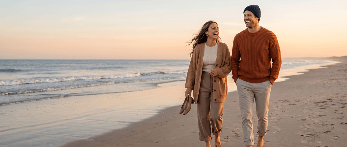 Couple walking on a beach at sunset in a camel cardigan and a rust crewneck sweater
