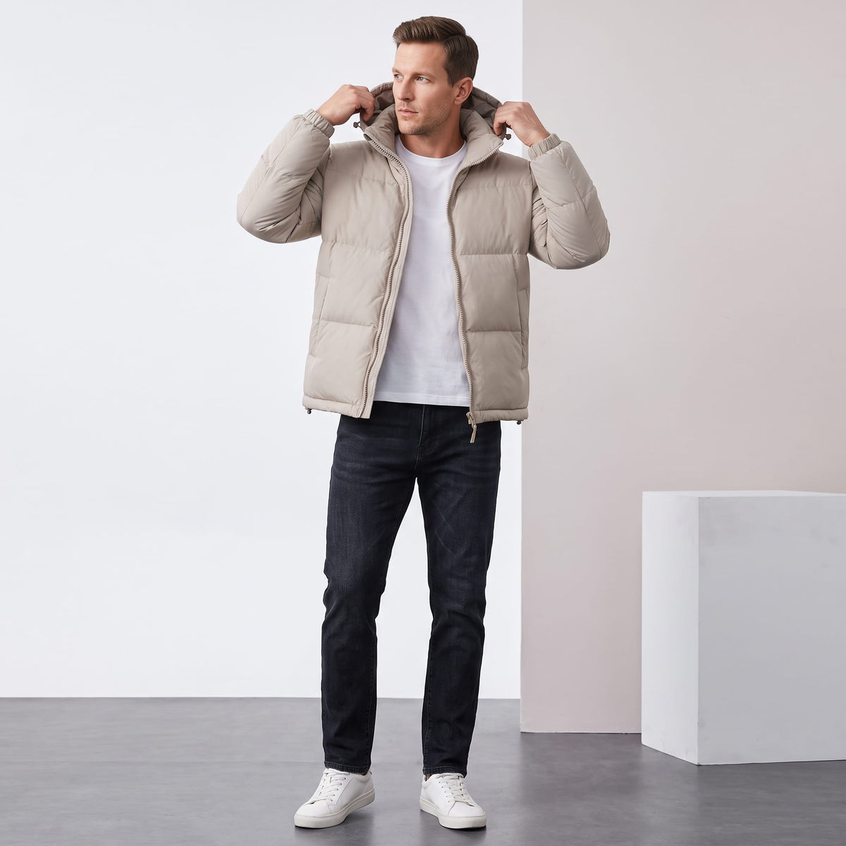 Man adjusting the hood of a beige Salvador insulated puffer jacket with jeans, full-length view