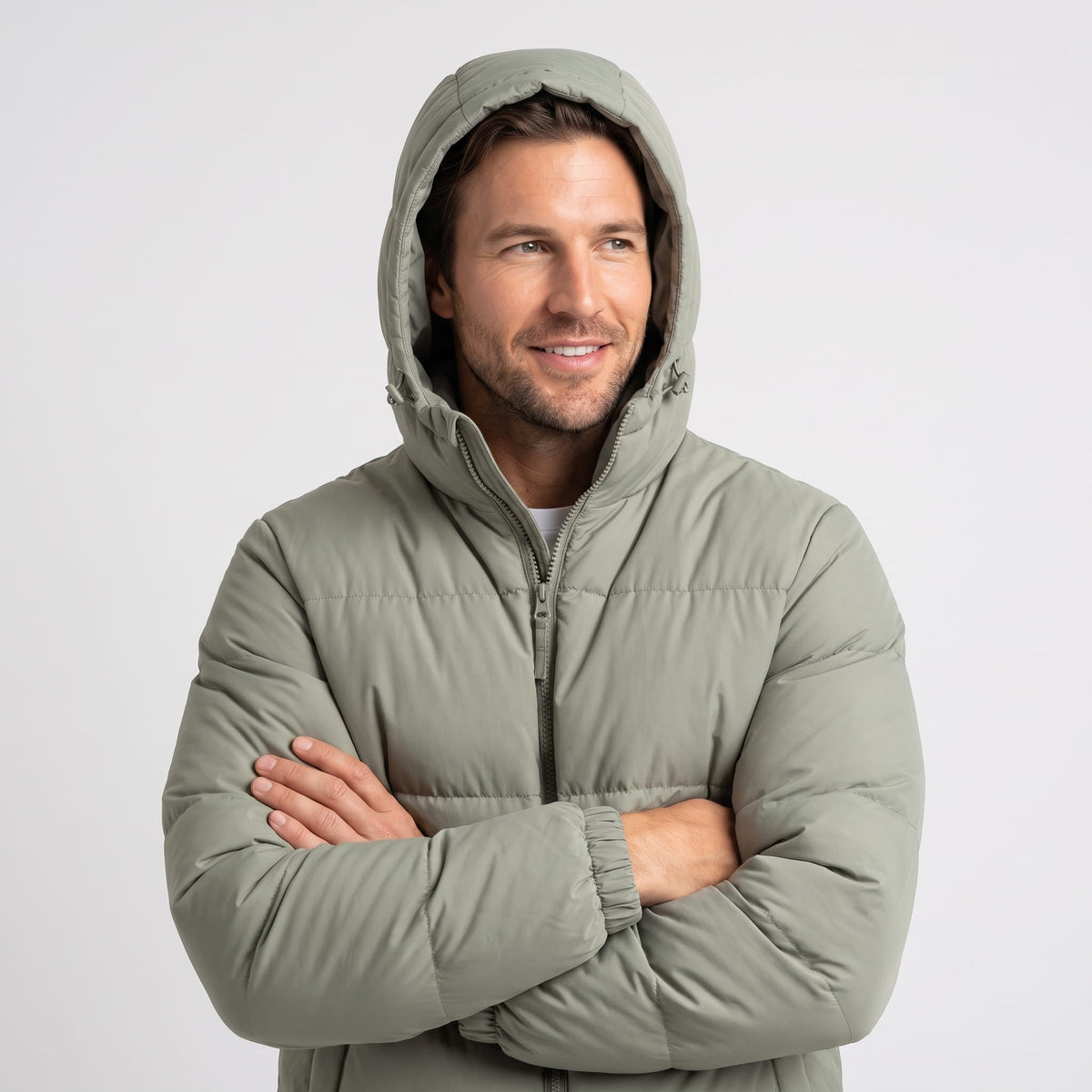 Man wearing sage Salvador insulated puffer jacket with the hood up, arms crossed