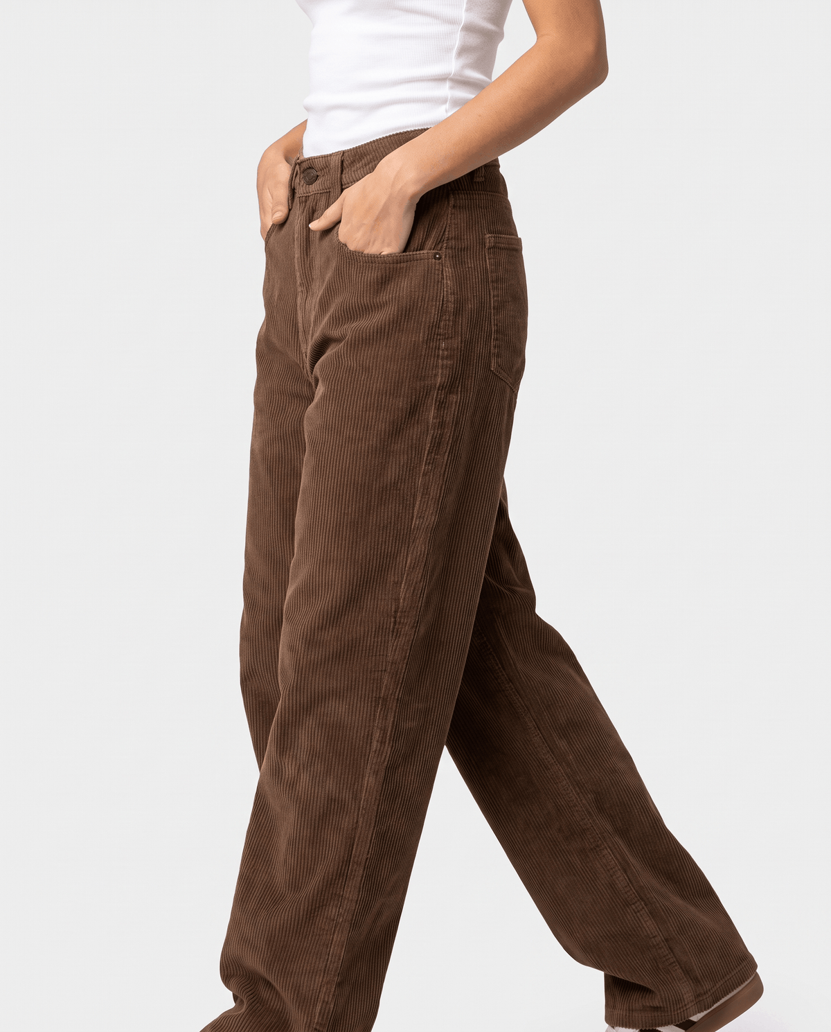 Side profile of chocolate ribbed trousers mid-stride showing the loose, slouchy leg