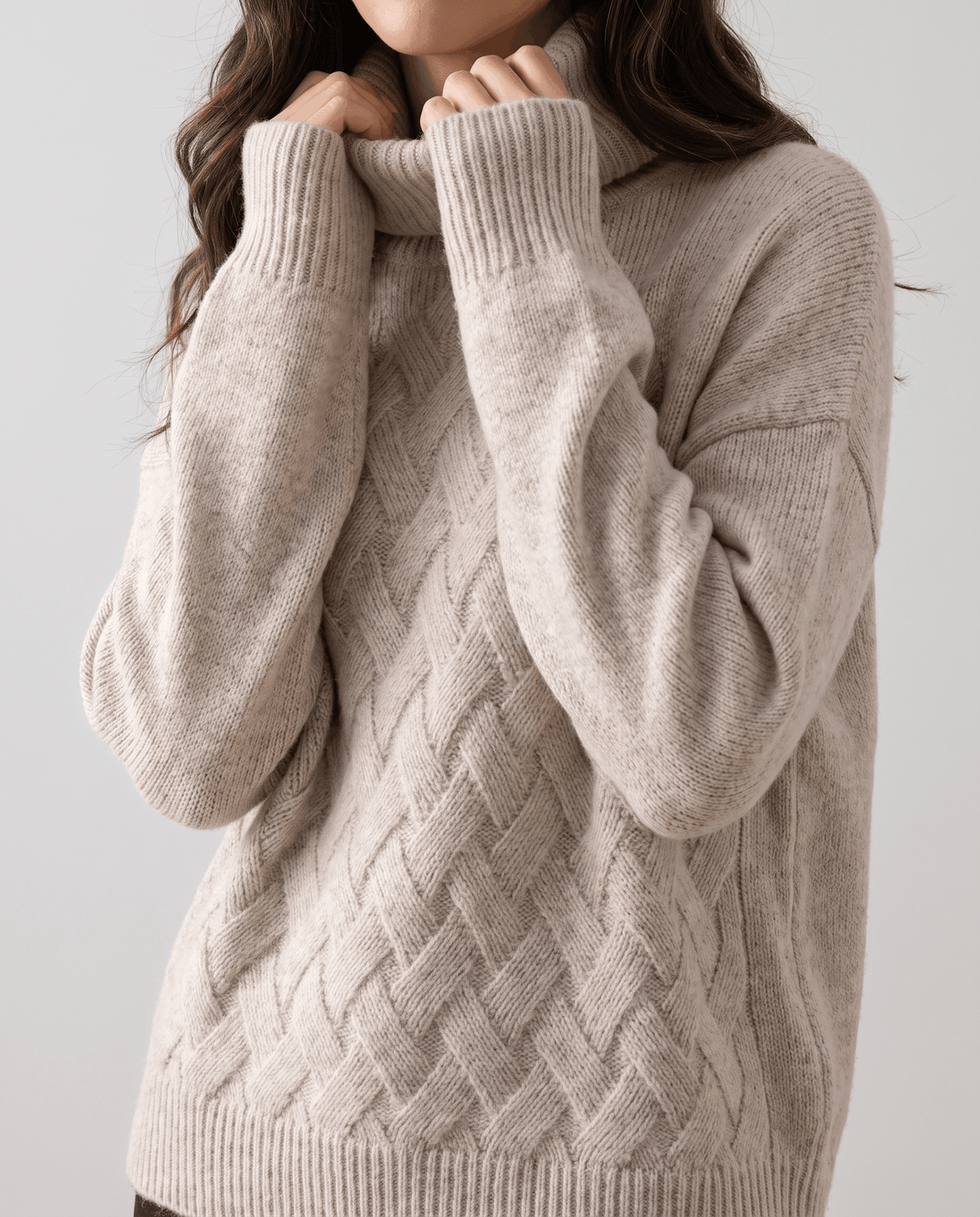 Model pulling up the folded collar of a beige basketweave sweater