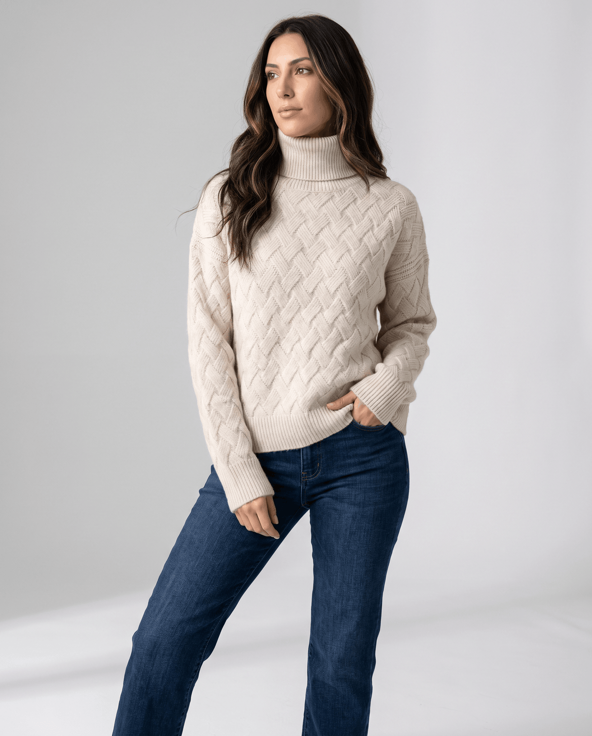 Woman wearing a cream basketweave knit turtleneck sweater with dark wash jeans