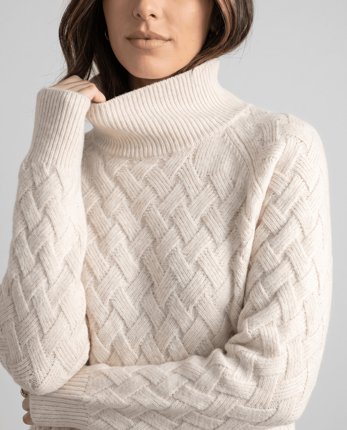 Cropped front view of cream turtleneck with crossing knit panels and ribbed cuffs