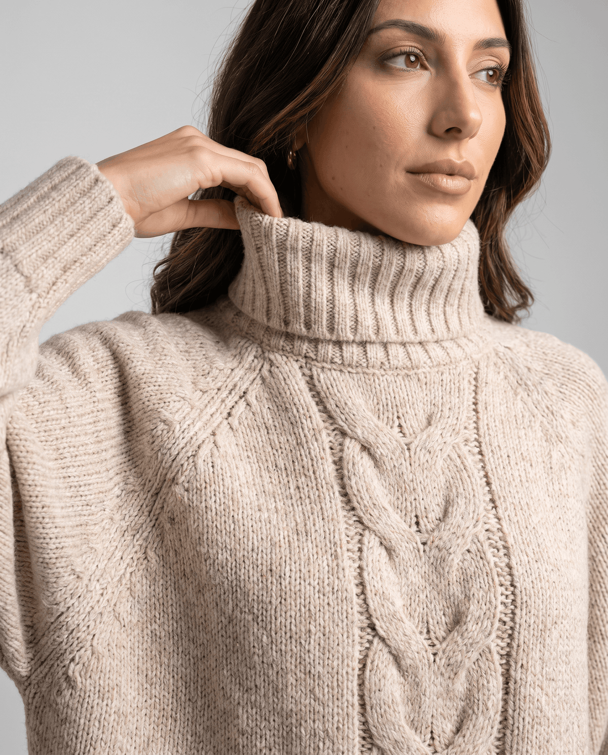 Model touching the folded collar of an oatmeal beige chunky sweater