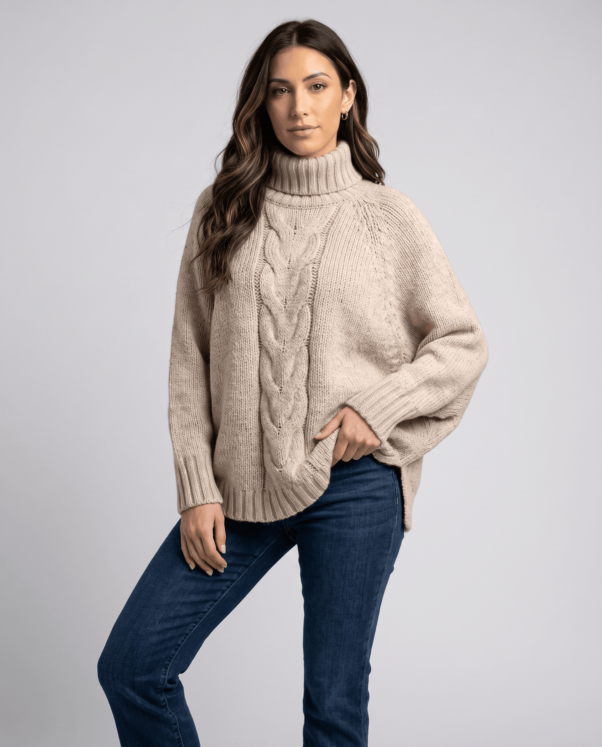 Front view of beige cable knit turtleneck worn with dark wash jeans