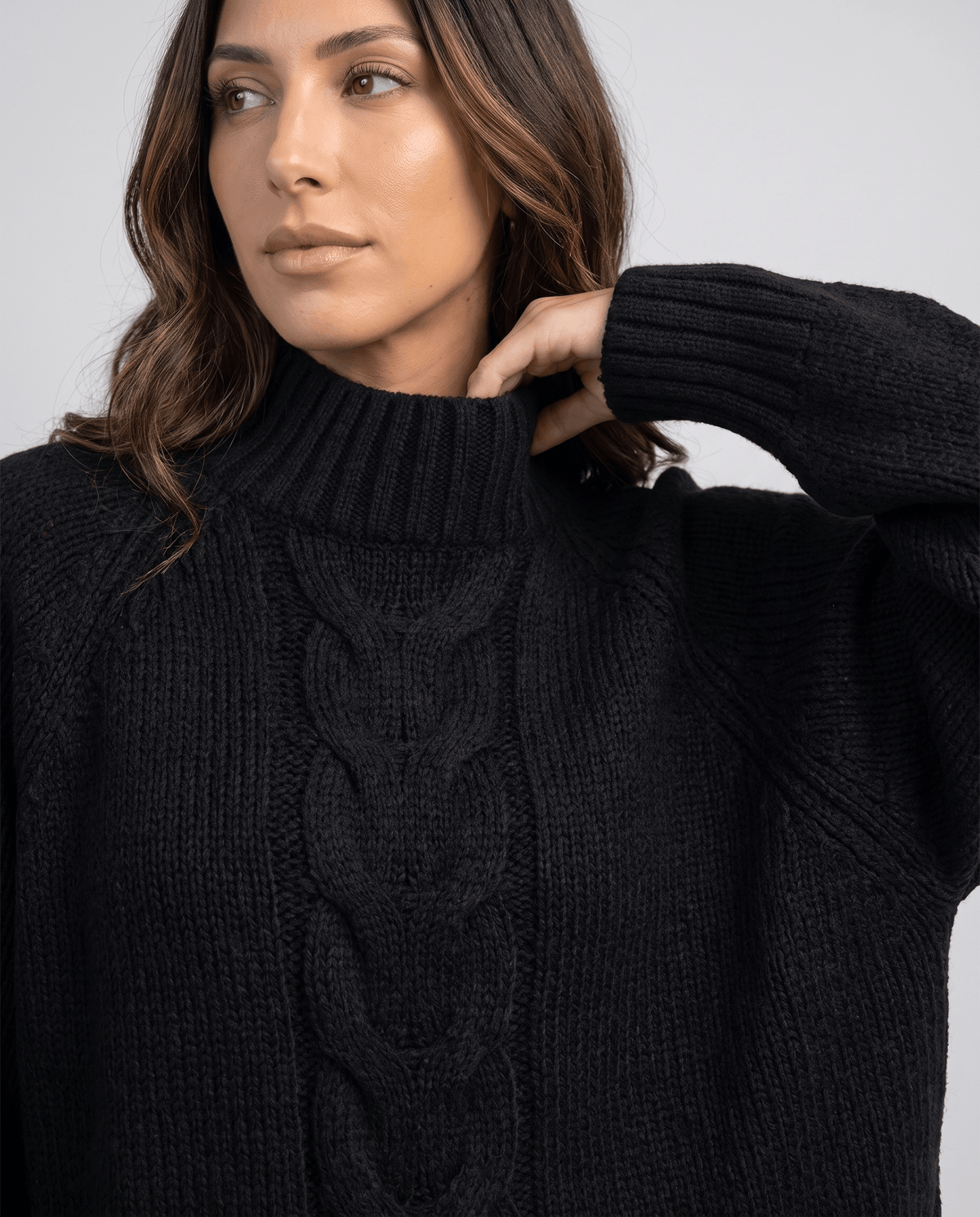 Close-up of model at the collar of a black chunky cable sweater