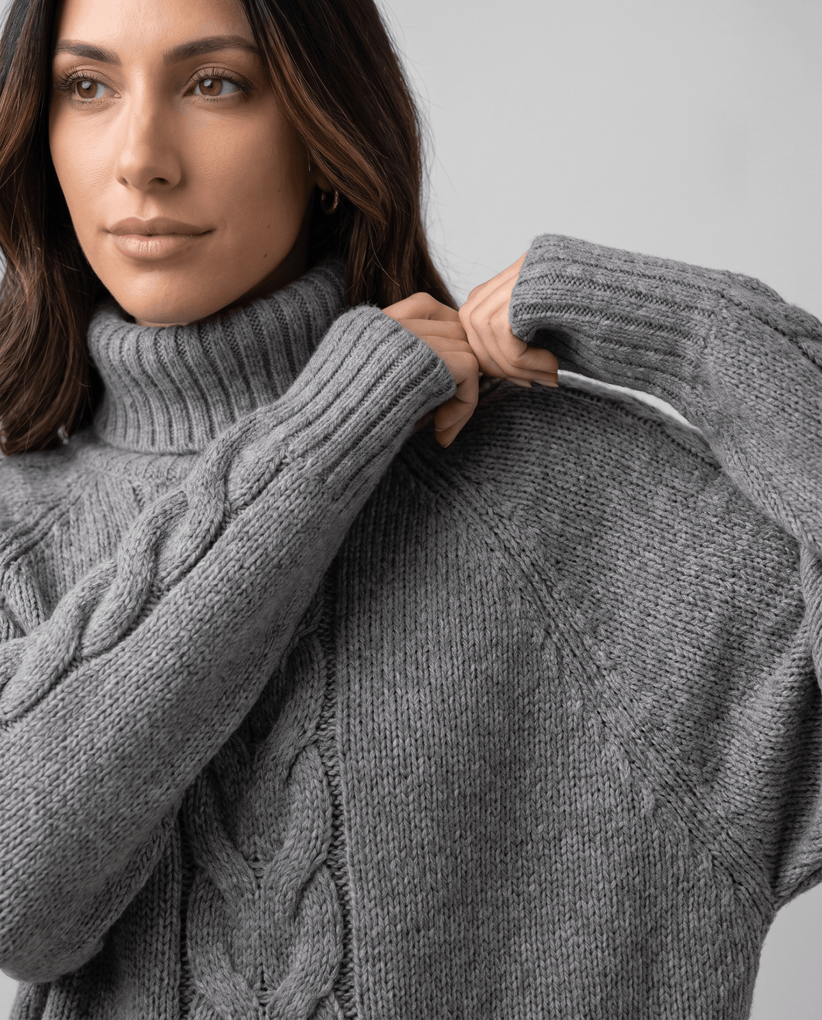 Model adjusting the folded collar of a gray chunky knit sweater