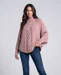 Woman wearing a pink batwing cable knit turtleneck sweater with medium wash jeans