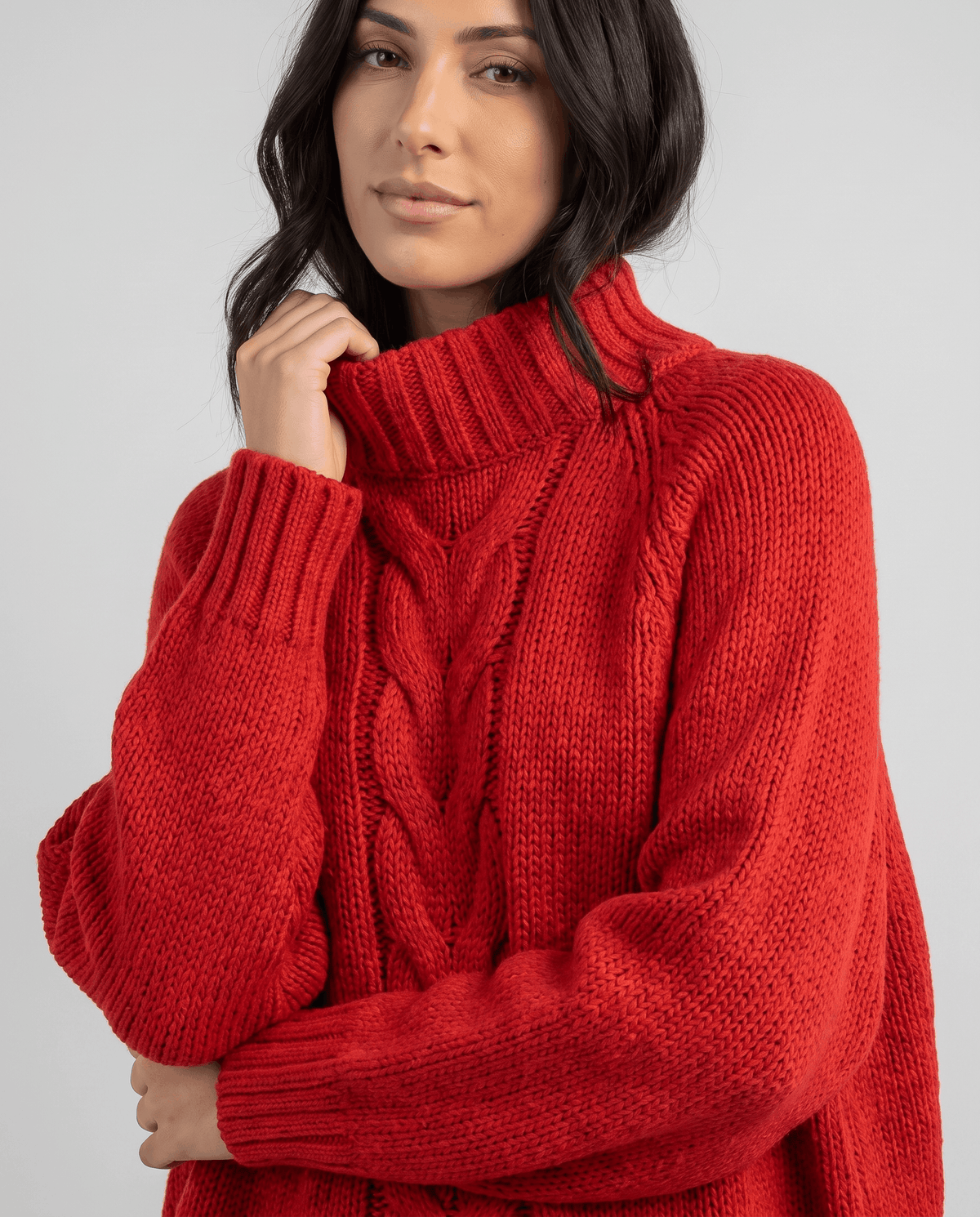 Model touching the folded collar of a red chunky cable turtleneck
