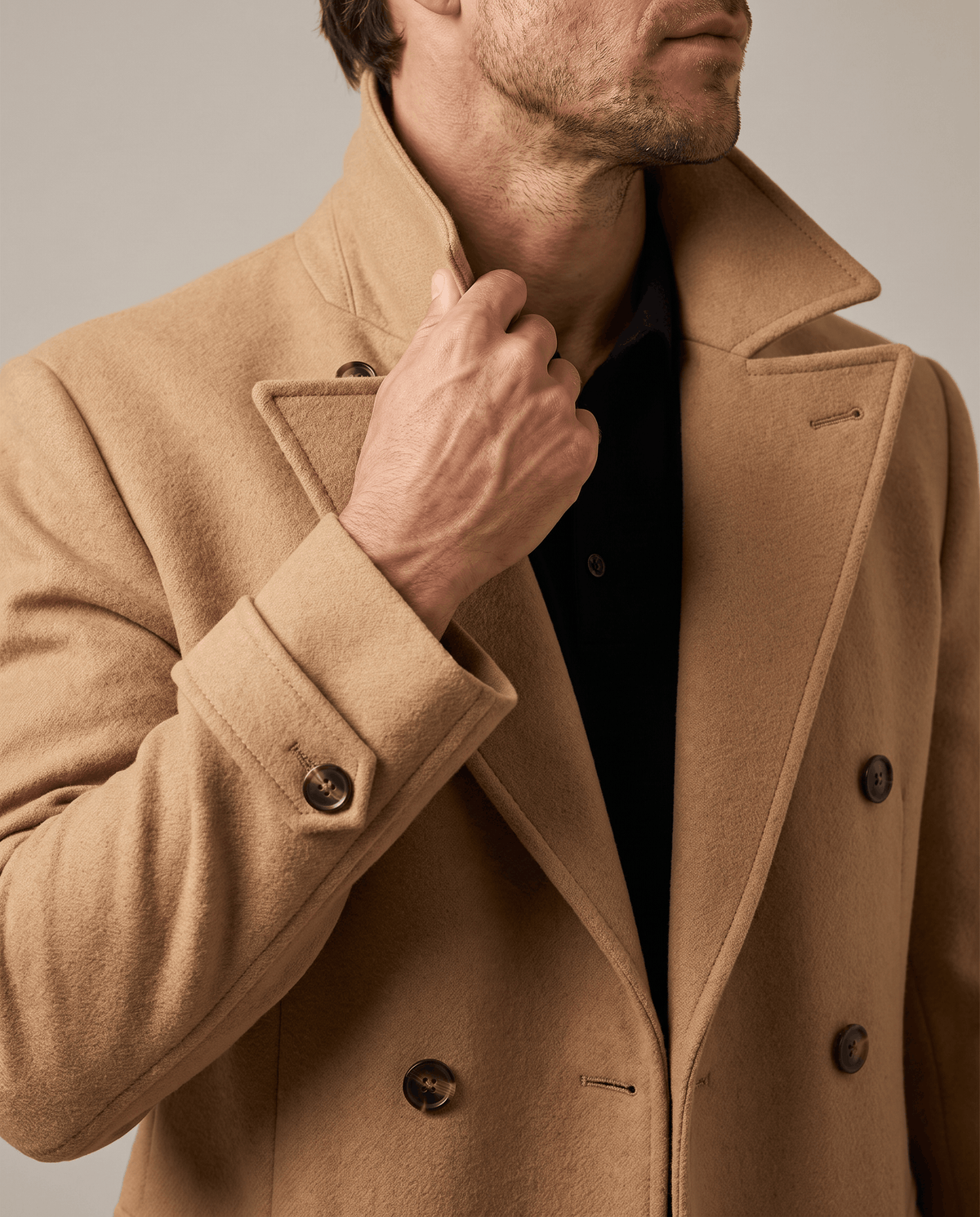 Close-up of beige wool coat collar and double-breasted buttons with a hand at the lapel