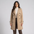 Woman in beige belted double-breasted trench coat over a cream turtleneck and brown trousers