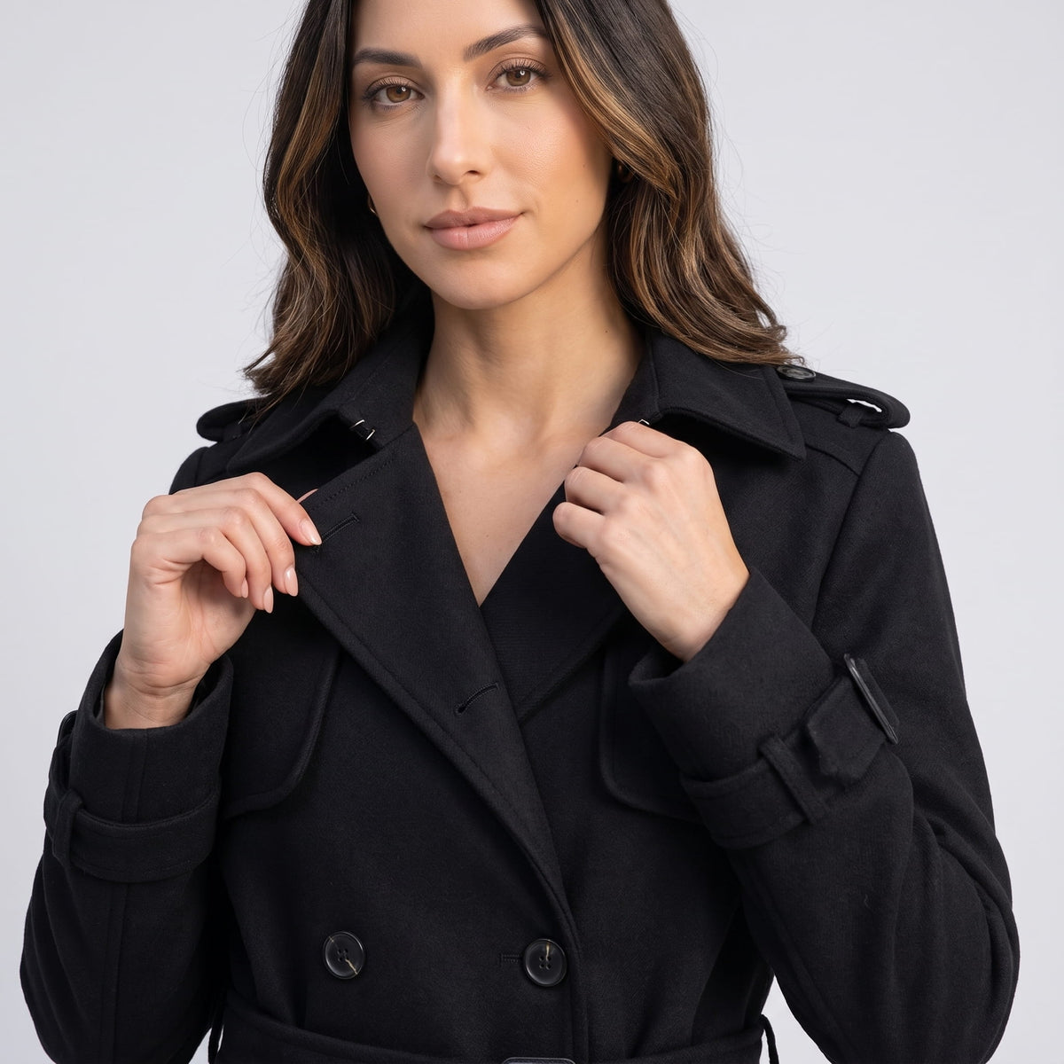 Model holding the wide lapels of a black coat, close-up view