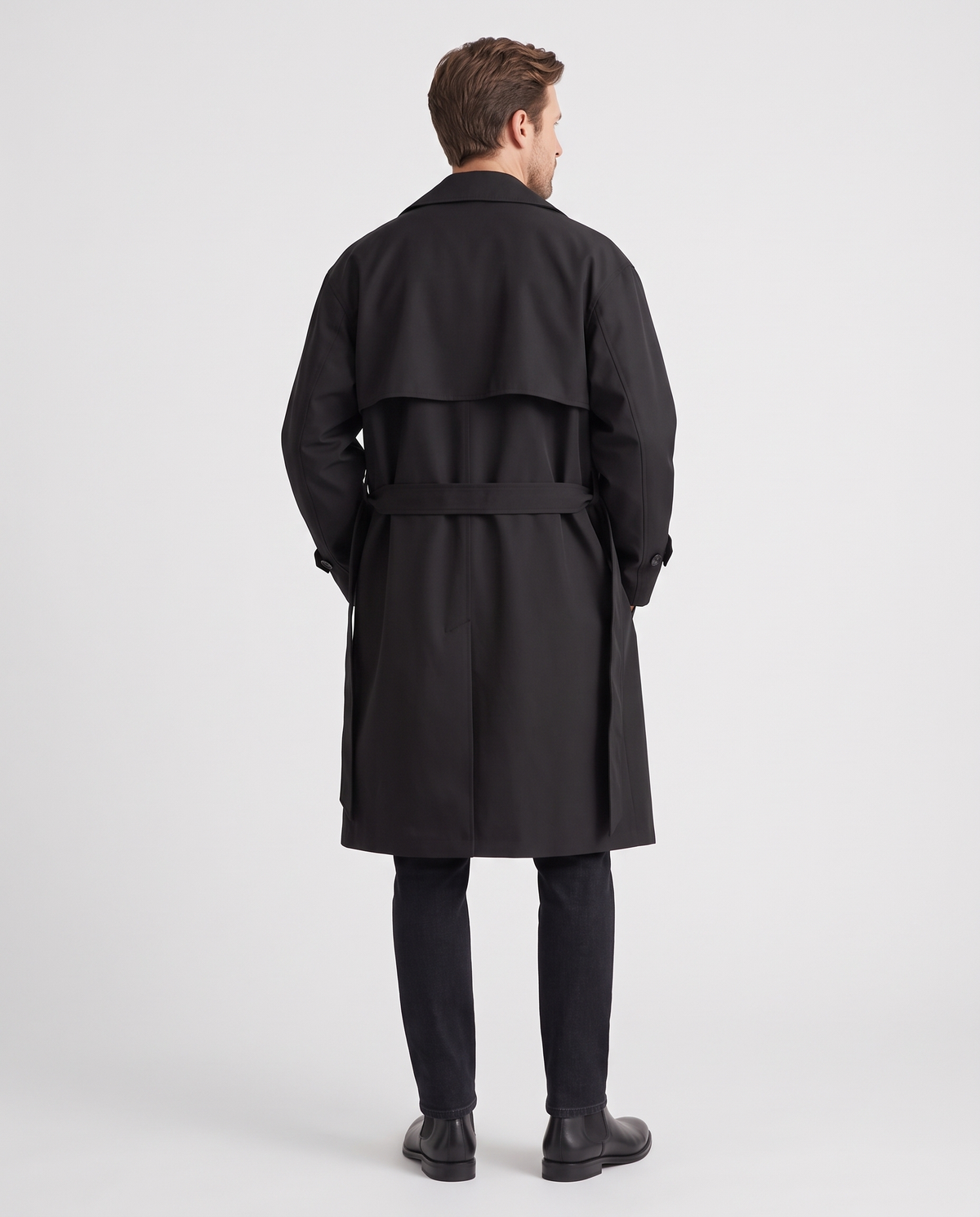 Back view of black trench coat with storm flap and tie belt, worn with black trousers