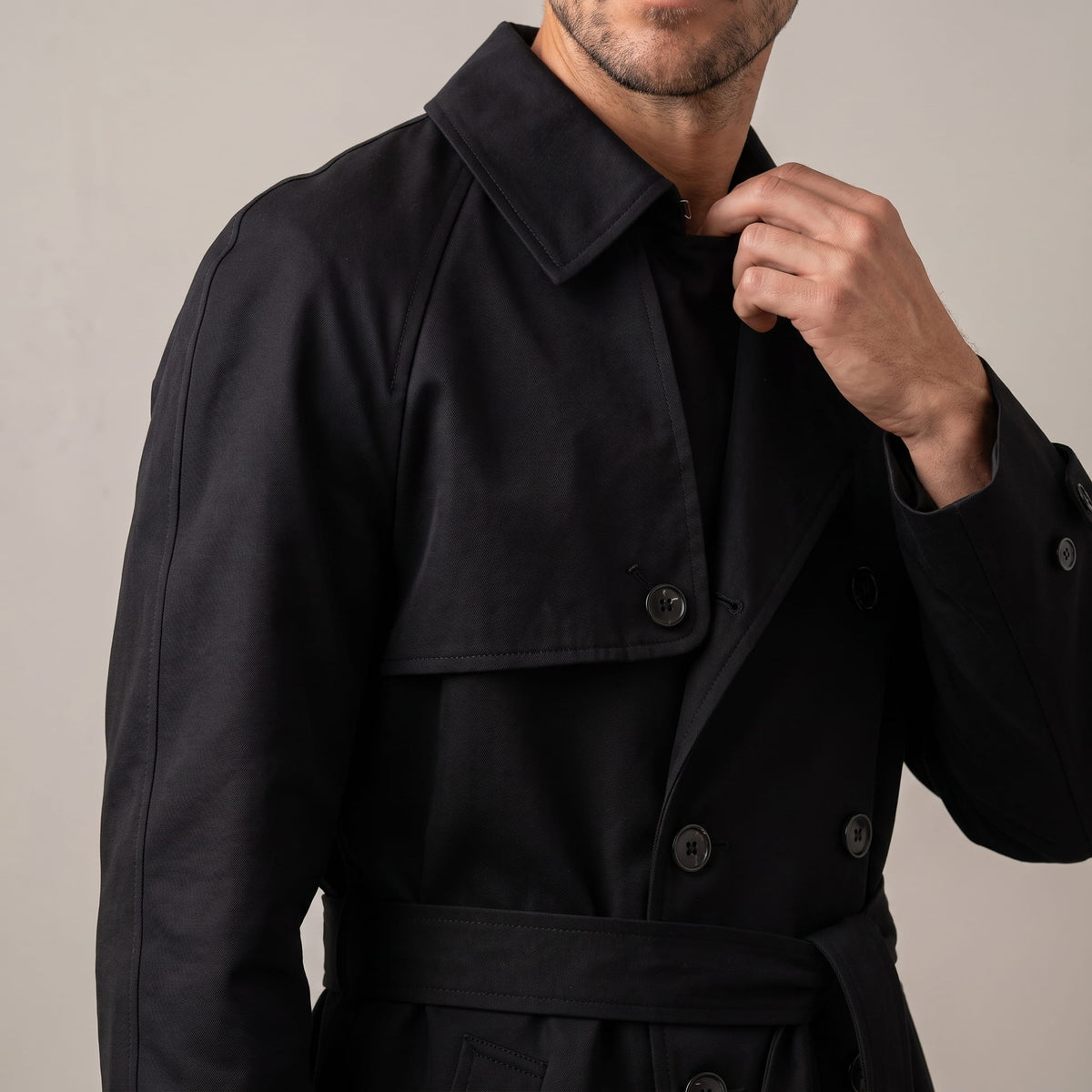 Close-up of black trench coat collar and storm flap, model adjusting the collar