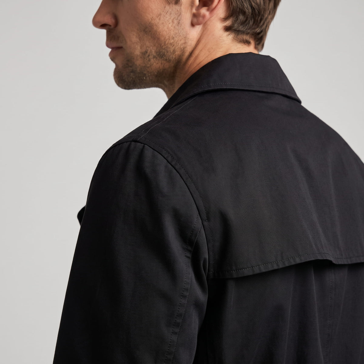 Close-up of black trench coat storm flap and shoulder from behind