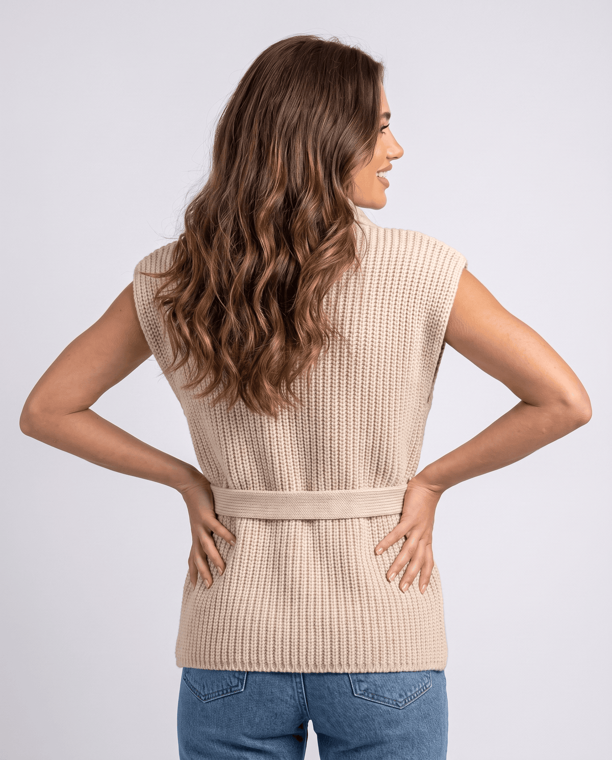 Back view of beige quilted vest with tie belt at waist, worn with jeans