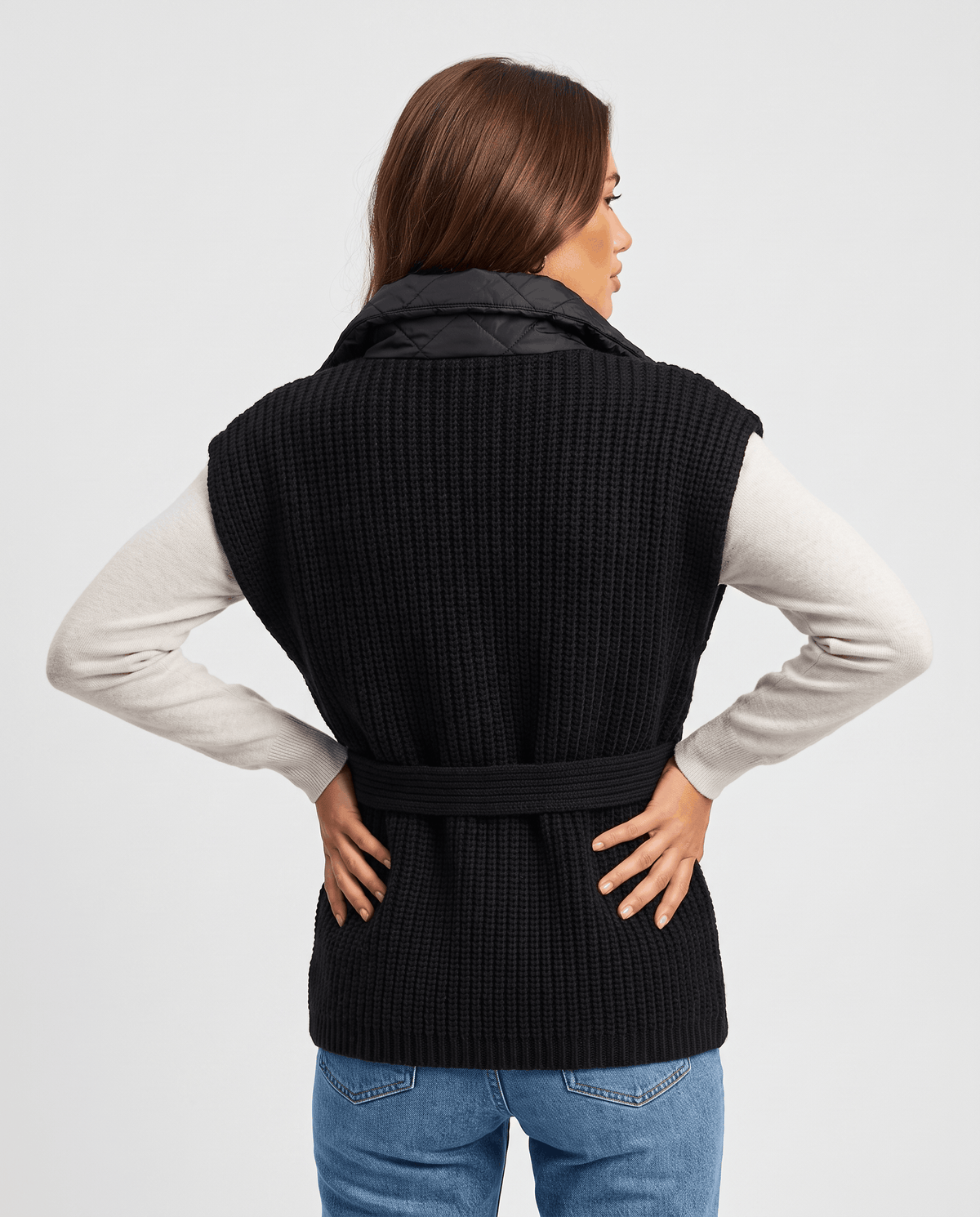 Back view of black quilted vest with belt tied at waist, hands on hips