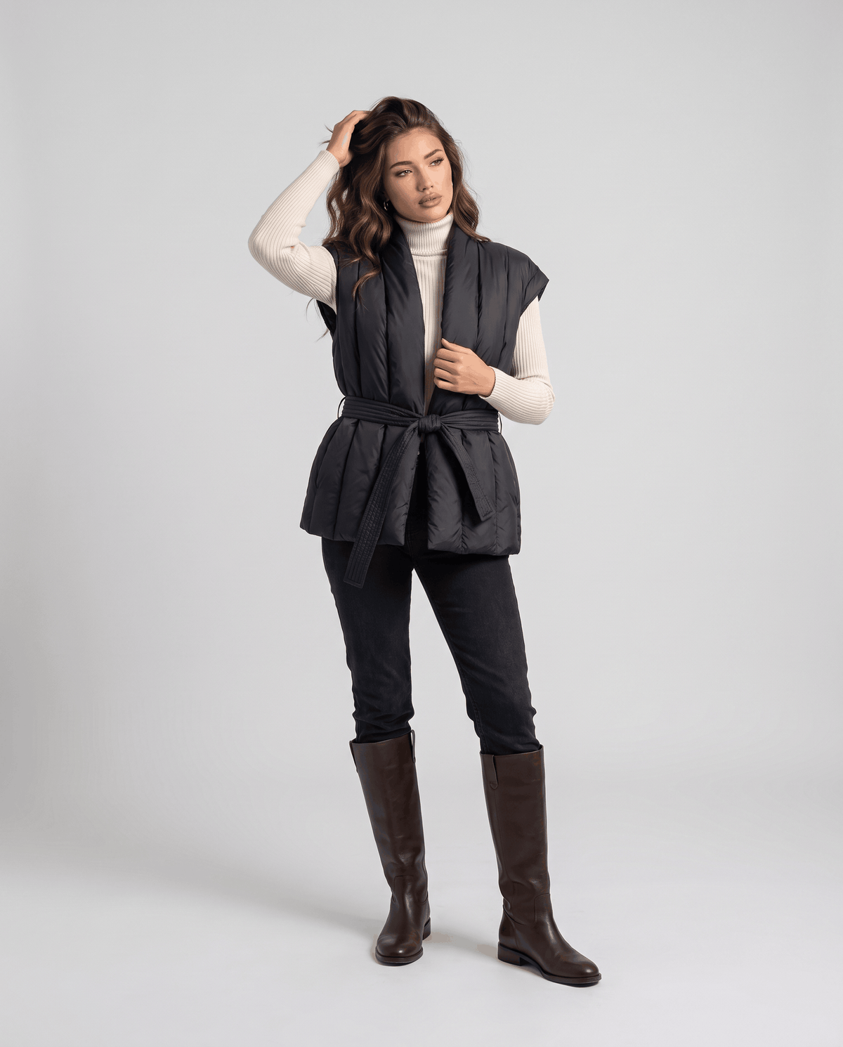 Full-length black vest belted at waist, styled with jeans and black boots