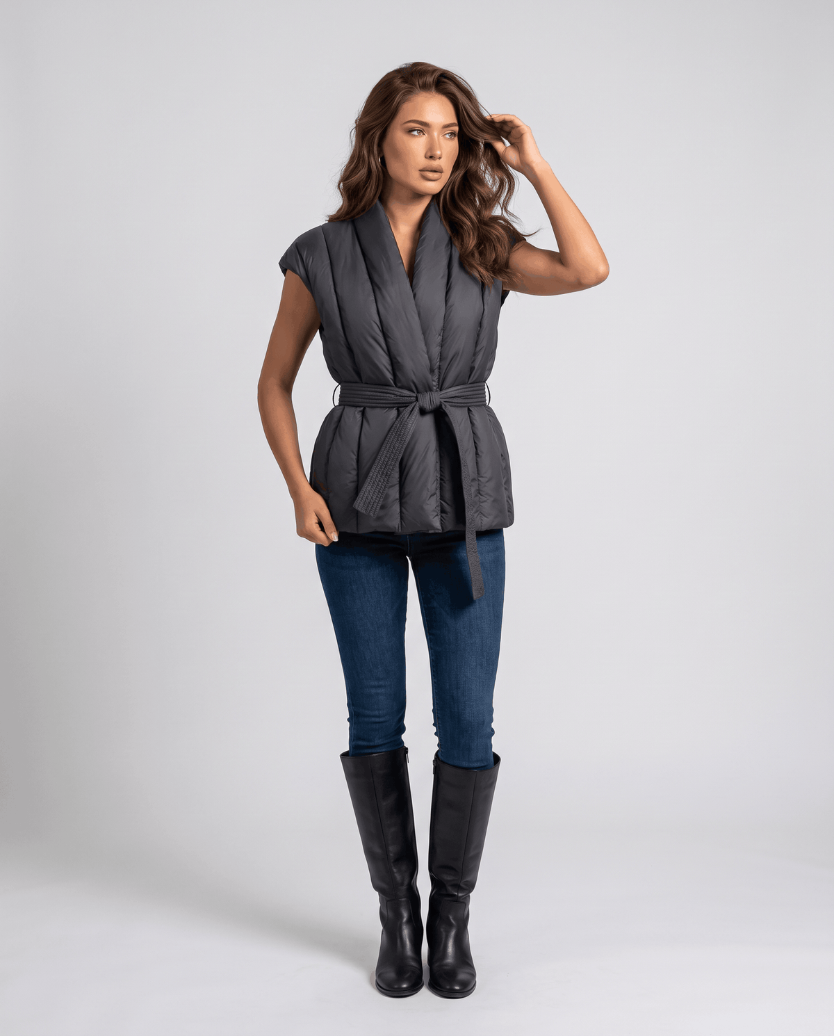 Full-length black quilted vest with tie belt, worn with blue jeans