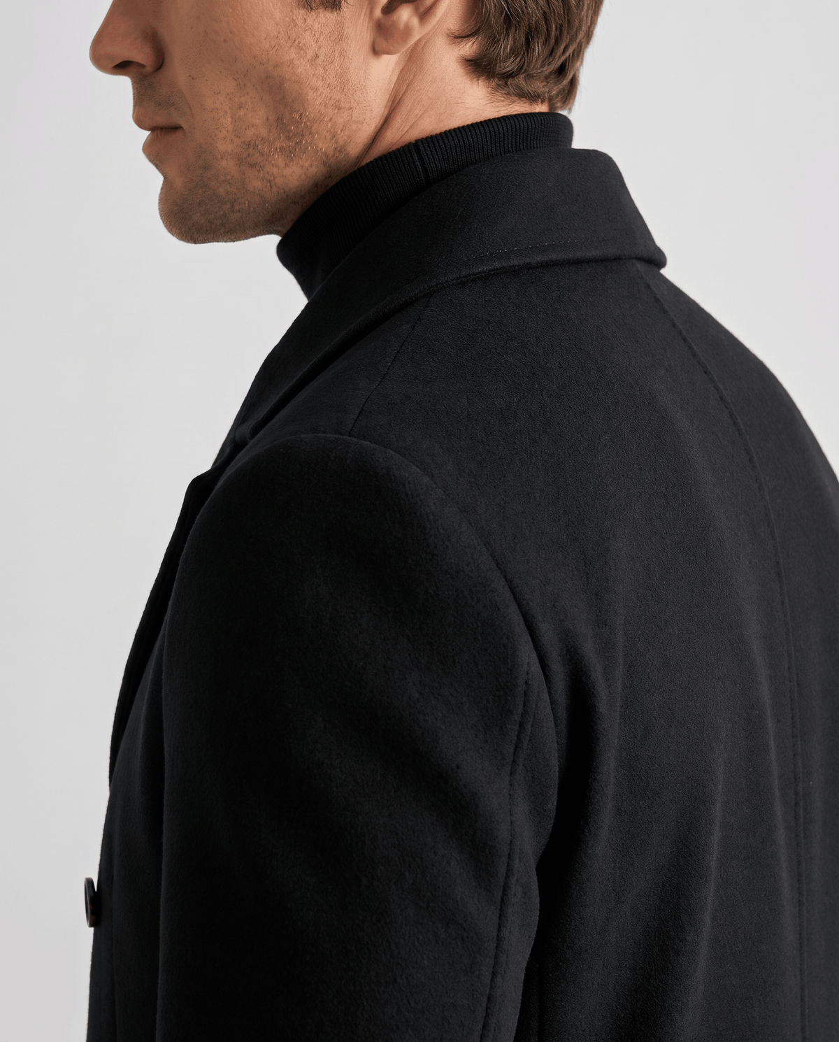 Side detail of a black wool coat worn over a black turtleneck